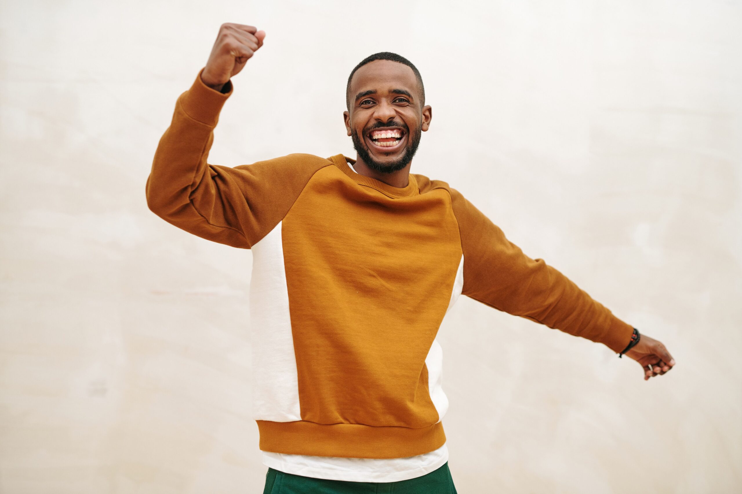 Cheerful African American man in a sweater celebrating with a big smile and arms raised.